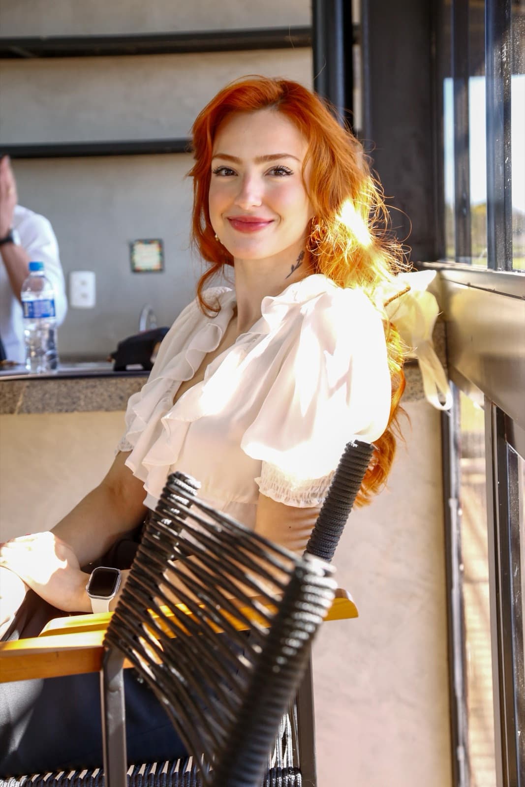 Me sitting at a counter in a white blouse, smiling with the late-afternoon light in my hair.